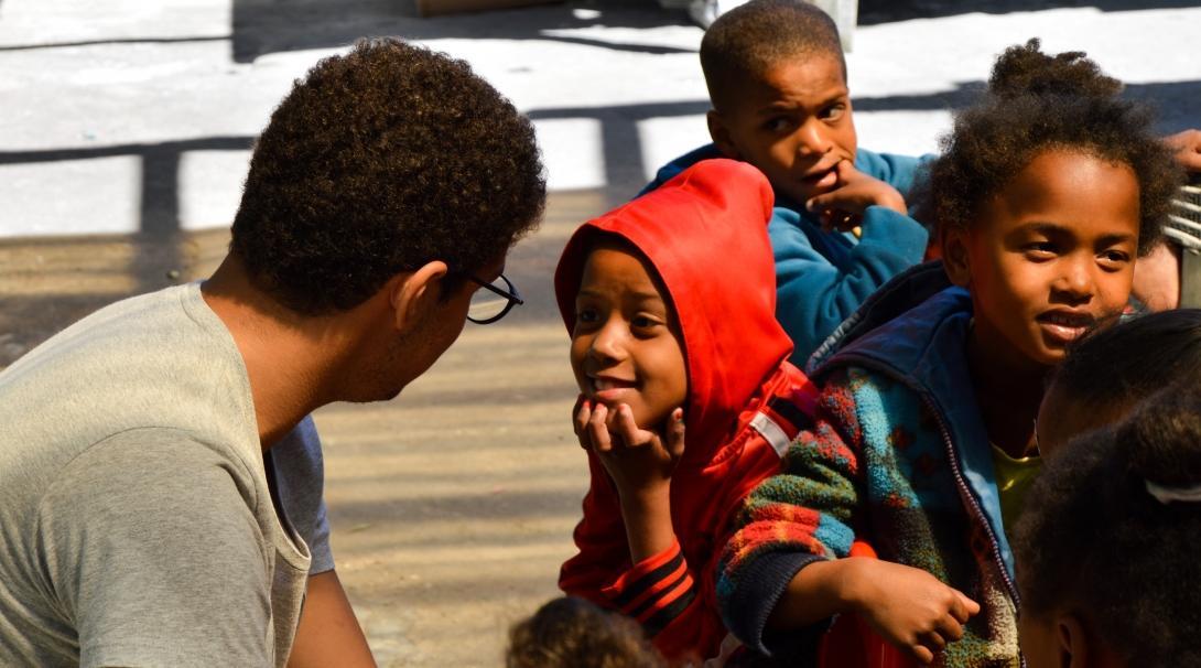 A high school student volunteering with children in South Africa speaks to a local child A student spends his summer vacation volunteering with children in South Africa as part of Projects Abroad's placement for teenagers
